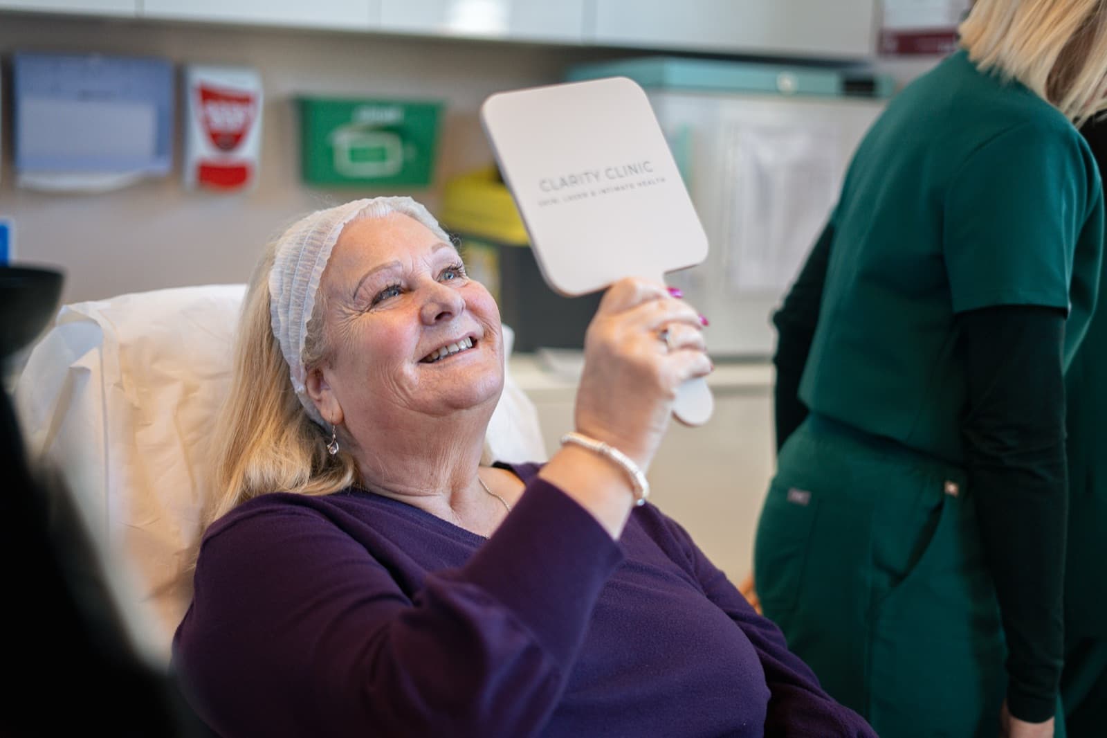 A smiling client admiring her skin in a hand mirror at Clarity Clinic Bedford